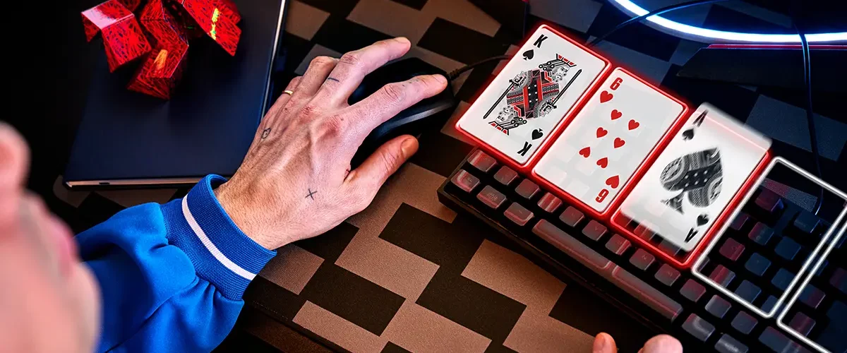 A close-up of a poker player’s hand on a mouse with digital playing cards over the keyboard, representing online poker decision-making.
