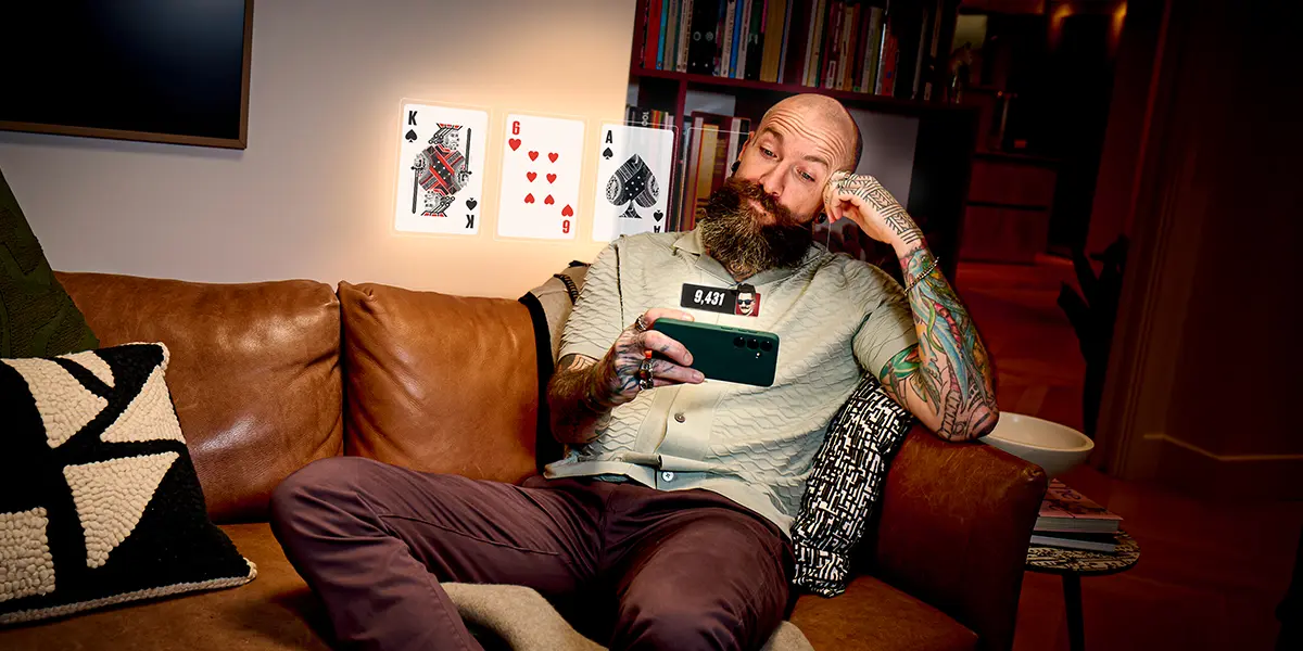 A man sitting on a couch, looking at a poker game on his phone with floating cards and chip counts, illustrating psychological focus and instinct-based play.