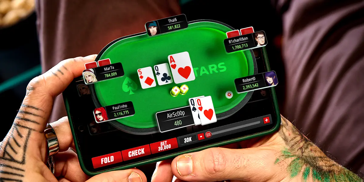A close-up shot of a player's hands holding a smartphone displaying an online poker tournament on PokerStars.